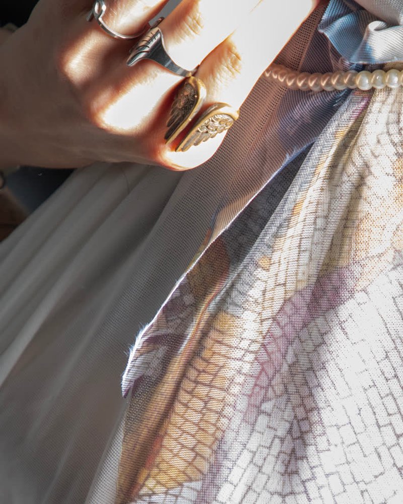 cyberbirdxx, a hand ringed in silver and gold on sheer printed fabric, a string of pearls at the gather